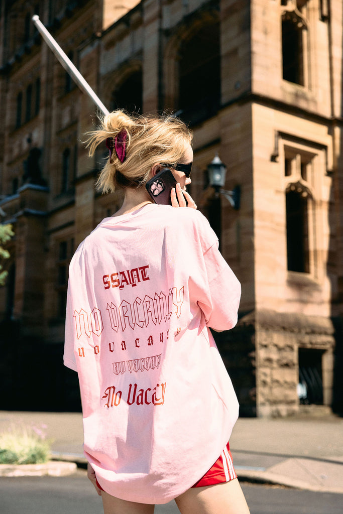 Person wearing a pink oversized shirt with text on the back, standing in an urban setting.